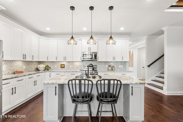 kitchen featuring decorative light fixtures, an island with sink, white cabinets, and appliances with stainless steel finishes