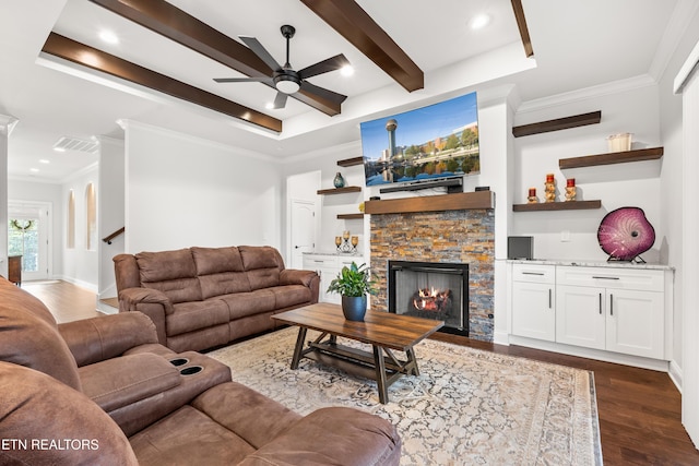 living room featuring hardwood / wood-style flooring, ceiling fan, a tray ceiling, ornamental molding, and a stone fireplace