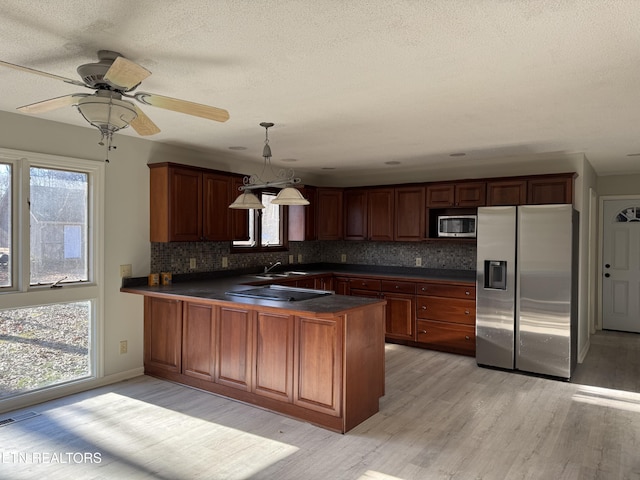 kitchen with a peninsula, appliances with stainless steel finishes, light wood-type flooring, backsplash, and dark countertops