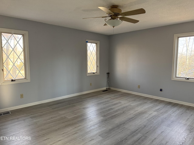 spare room featuring a textured ceiling, wood finished floors, a ceiling fan, visible vents, and baseboards