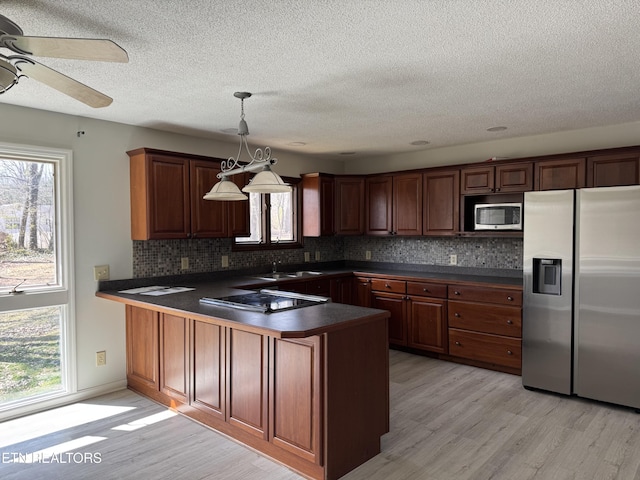 kitchen with dark countertops, light wood-style floors, a peninsula, and appliances with stainless steel finishes