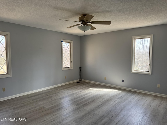 empty room with baseboards, ceiling fan, wood finished floors, and a healthy amount of sunlight