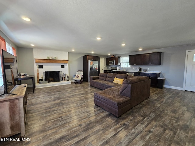 living room with a brick fireplace, a textured ceiling, and dark hardwood / wood-style flooring