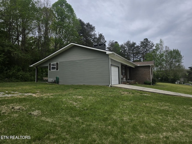 view of side of home with an attached garage, a lawn, a chimney, and concrete driveway