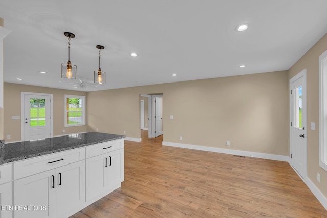 kitchen featuring light wood finished floors, baseboards, white cabinets, decorative light fixtures, and dark stone countertops
