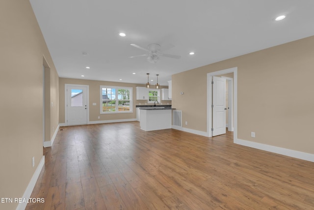 unfurnished living room featuring wood-type flooring, a ceiling fan, baseboards, recessed lighting, and a sink