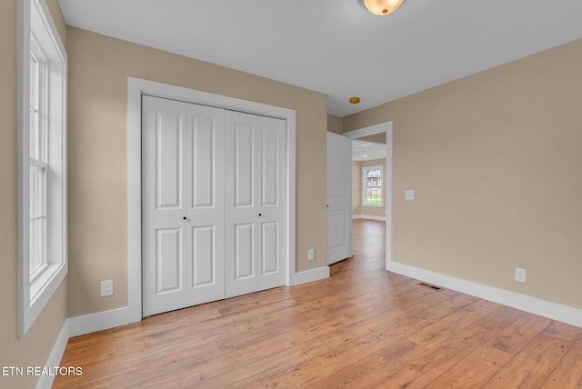 unfurnished bedroom featuring baseboards, light wood finished floors, and a closet