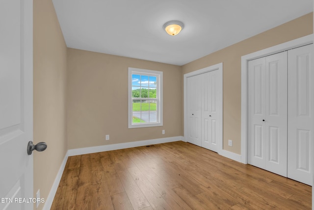 unfurnished bedroom with baseboards, multiple closets, and hardwood / wood-style floors