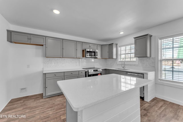 kitchen with gray cabinets, stainless steel appliances, a center island, sink, and light hardwood / wood-style flooring