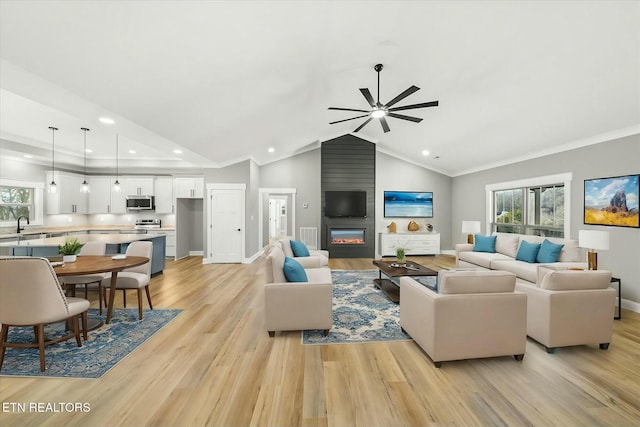 living room with ceiling fan, ornamental molding, light hardwood / wood-style floors, a large fireplace, and vaulted ceiling