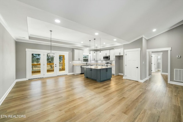 kitchen featuring hanging light fixtures, stainless steel appliances, a center island, white cabinets, and light wood-type flooring