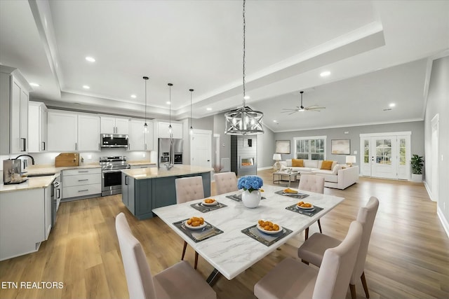 dining room featuring ornamental molding, a raised ceiling, sink, and light hardwood / wood-style flooring