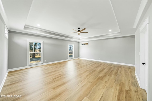 empty room with a raised ceiling, ceiling fan, and light wood-type flooring