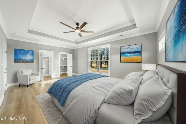 bedroom with ornamental molding, light hardwood / wood-style floors, a raised ceiling, and ceiling fan