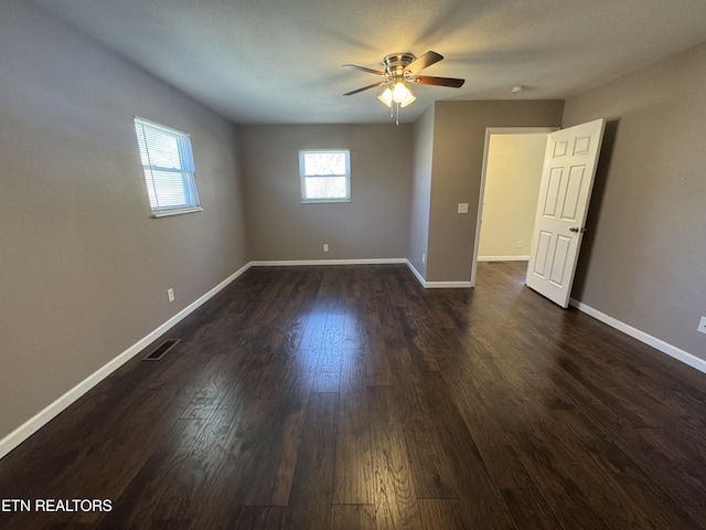 unfurnished room featuring dark wood-style floors, a ceiling fan, visible vents, and baseboards