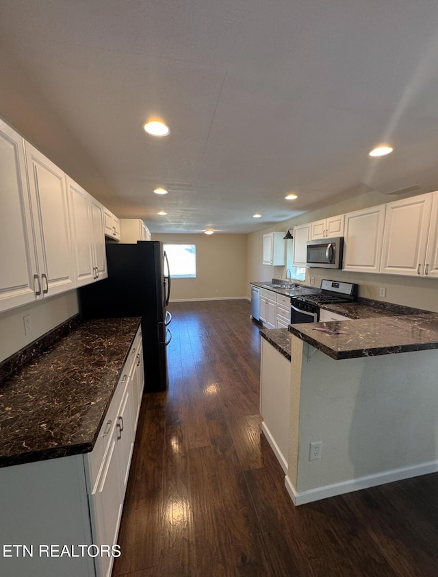 kitchen featuring dark stone counters, dark wood-style floors, appliances with stainless steel finishes, a peninsula, and white cabinetry