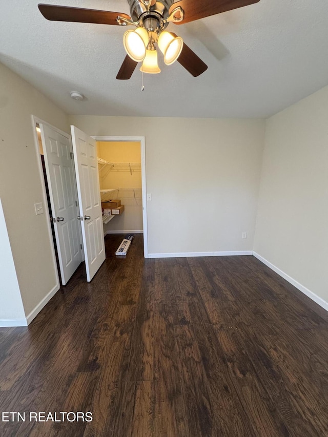 unfurnished bedroom with a textured ceiling, a spacious closet, baseboards, and wood finished floors