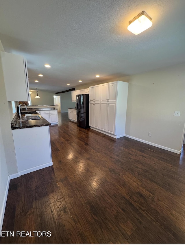 kitchen with baseboards, dark wood-style flooring, freestanding refrigerator, white cabinetry, and a sink