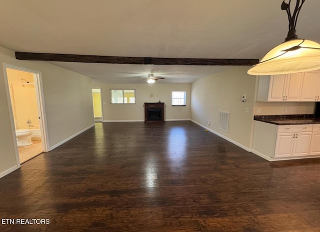 unfurnished living room featuring a fireplace, baseboards, dark wood-type flooring, and beam ceiling