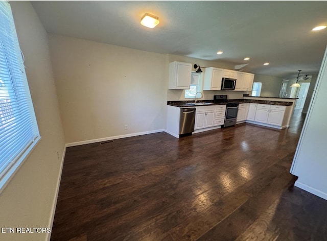 kitchen with dark countertops, appliances with stainless steel finishes, dark wood-type flooring, a peninsula, and a sink