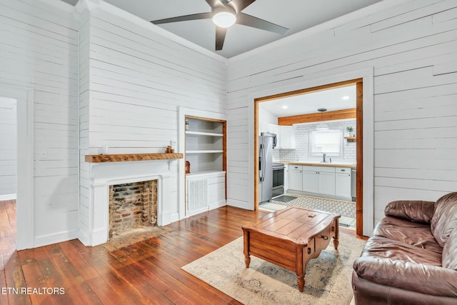 living room featuring wood-type flooring, sink, ceiling fan, and wooden walls