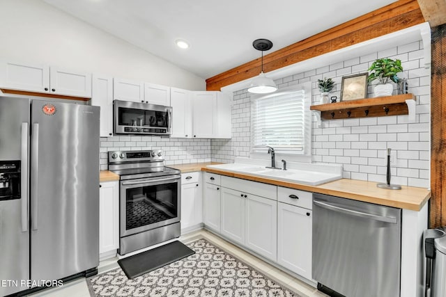 kitchen with lofted ceiling, stainless steel appliances, decorative light fixtures, and white cabinets