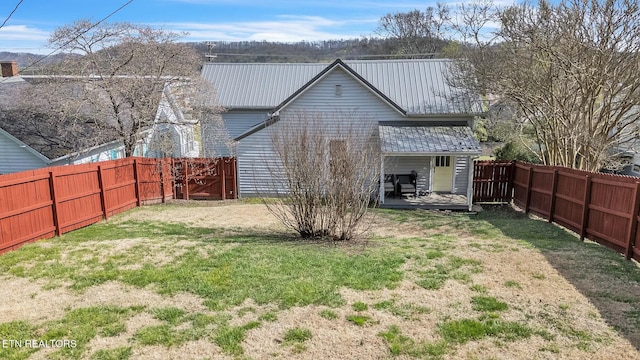 back of house featuring a fenced backyard, metal roof, and a lawn