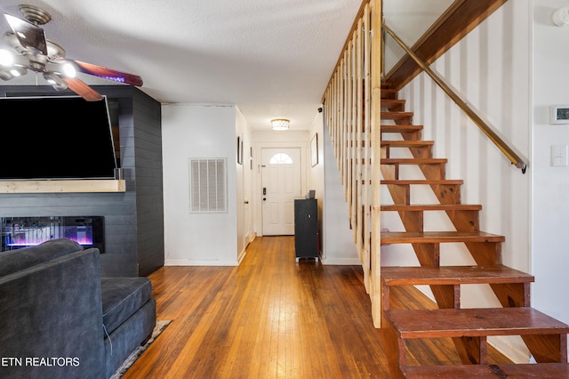 interior space featuring ceiling fan, a fireplace, a textured ceiling, and hardwood / wood-style floors