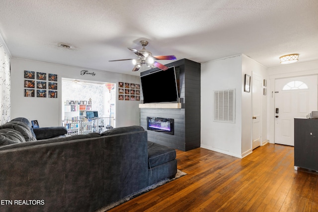 living room featuring a textured ceiling, dark wood-type flooring, a large fireplace, and ceiling fan