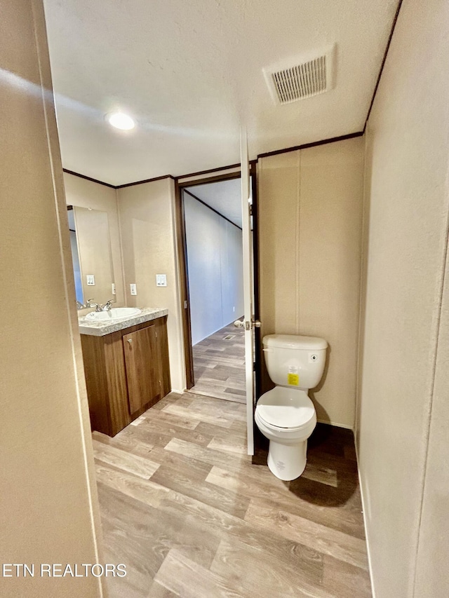 bathroom featuring toilet, ornamental molding, wood-type flooring, and vanity