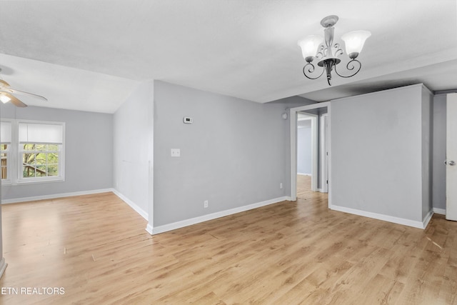 empty room with ceiling fan with notable chandelier, light wood-type flooring, and vaulted ceiling