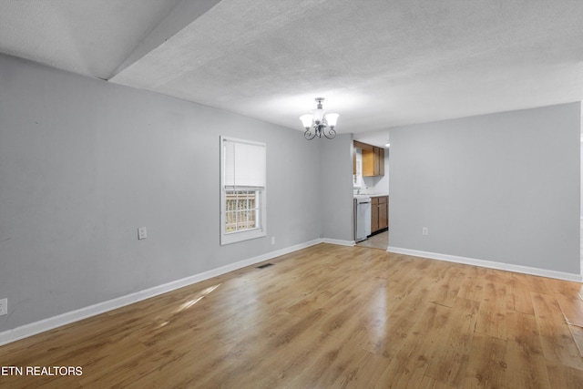 empty room featuring a textured ceiling, light wood-type flooring, and an inviting chandelier