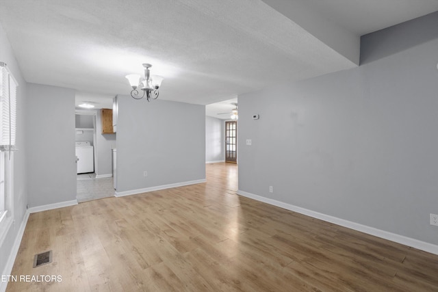 spare room featuring washer / clothes dryer, a textured ceiling, light wood-type flooring, and a notable chandelier