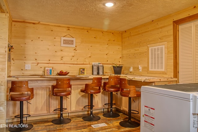 bar featuring a textured ceiling, dark hardwood / wood-style floors, and wood walls