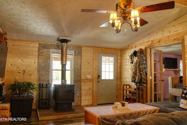 interior space with lofted ceiling, ceiling fan, wood walls, a wood stove, and a textured ceiling