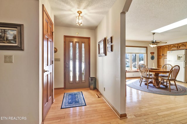 entrance foyer with ceiling fan, a textured ceiling, light hardwood / wood-style floors, and a skylight