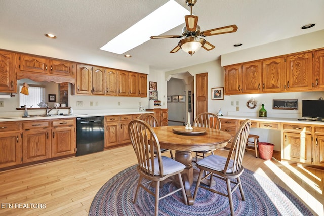 kitchen featuring sink, a skylight, black dishwasher, ceiling fan, and light hardwood / wood-style floors