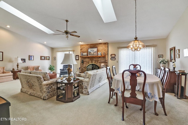 carpeted dining room featuring ceiling fan with notable chandelier, a fireplace, and vaulted ceiling with skylight