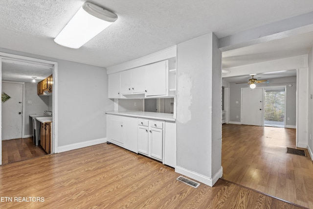 kitchen with a textured ceiling, ceiling fan, light hardwood / wood-style flooring, and white cabinetry