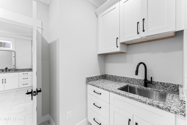 kitchen featuring light stone counters, sink, and white cabinets