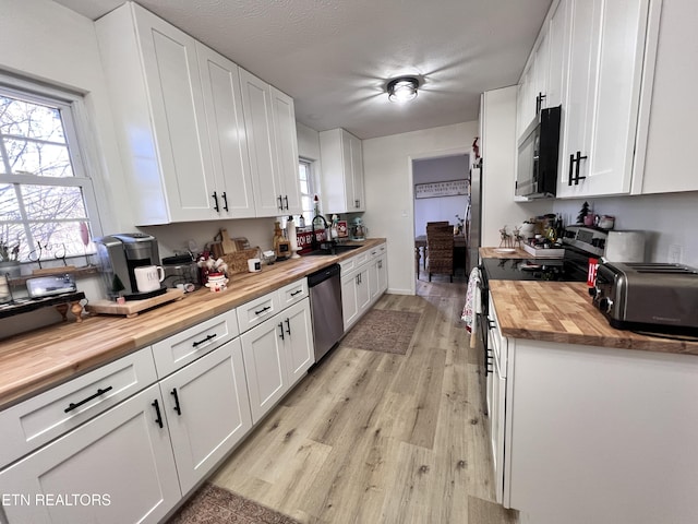 kitchen with stainless steel appliances, white cabinets, light hardwood / wood-style flooring, sink, and butcher block counters