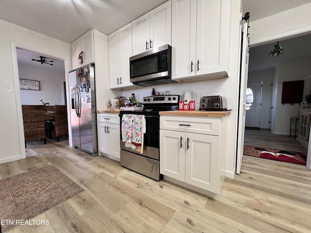 kitchen featuring butcher block counters, white cabinets, light wood-type flooring, and appliances with stainless steel finishes