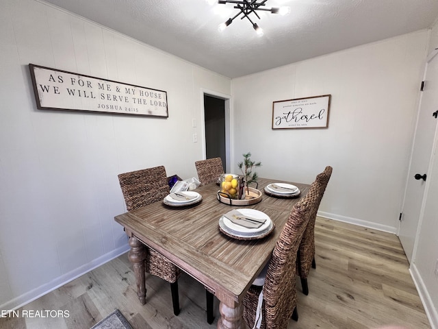 dining space featuring light wood-type flooring, a textured ceiling, and an inviting chandelier