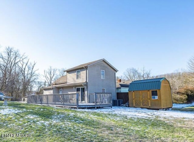 snow covered property featuring a storage unit, a deck, and a lawn