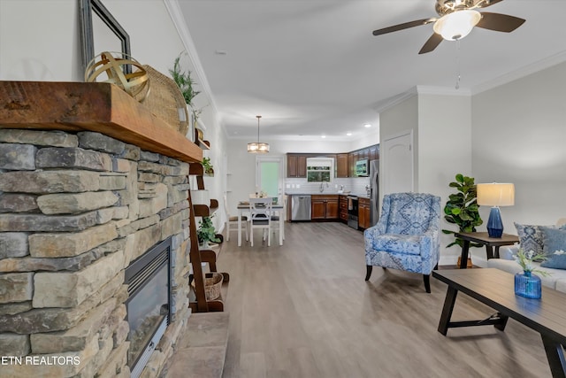 living room featuring ceiling fan, light wood-type flooring, crown molding, and a fireplace