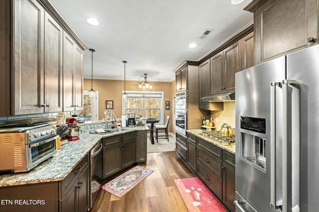 kitchen featuring appliances with stainless steel finishes, light hardwood / wood-style floors, decorative backsplash, hanging light fixtures, and dark brown cabinets