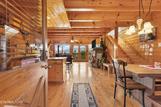 dining room featuring ceiling fan with notable chandelier, wooden walls, wooden ceiling, light hardwood / wood-style flooring, and beam ceiling