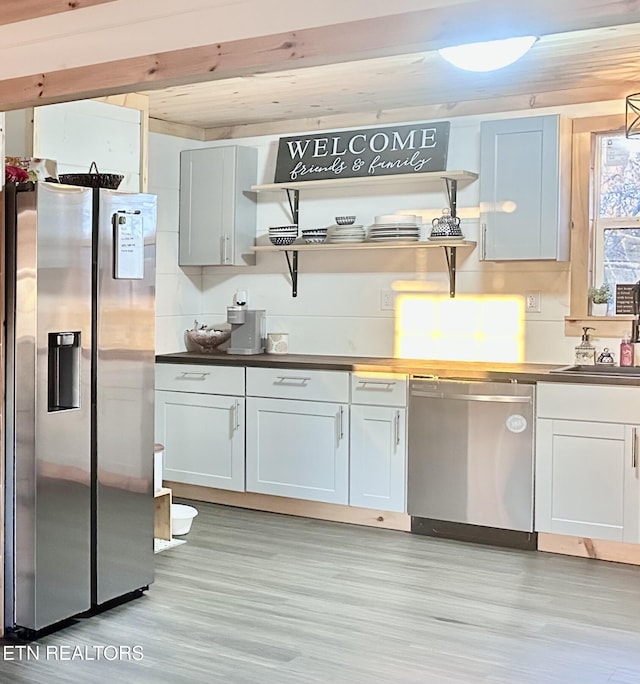 kitchen with appliances with stainless steel finishes, white cabinetry, light hardwood / wood-style floors, sink, and backsplash