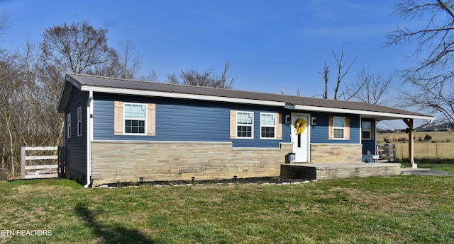 view of front facade with a front lawn, fence, stone siding, and metal roof