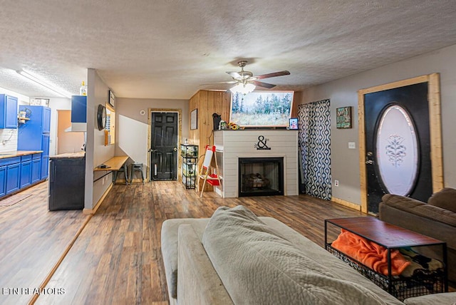 living room with a textured ceiling, a brick fireplace, dark hardwood / wood-style floors, and ceiling fan